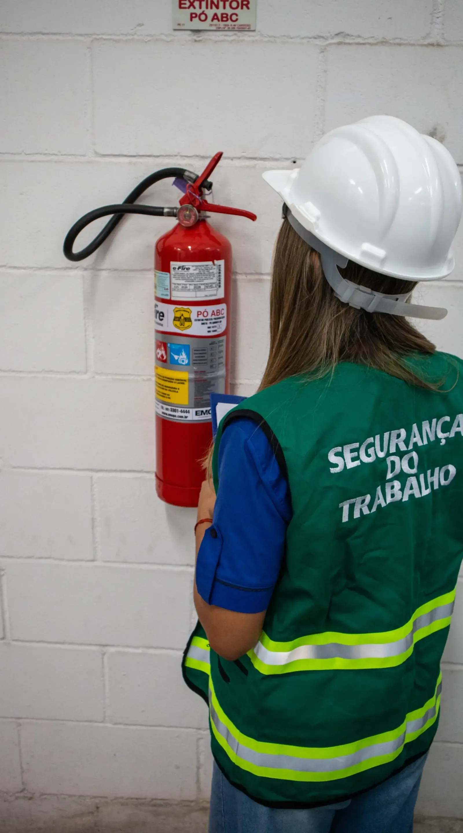 Colaboradora de segurança do trabalho JAM examinando extintor de incêndio
